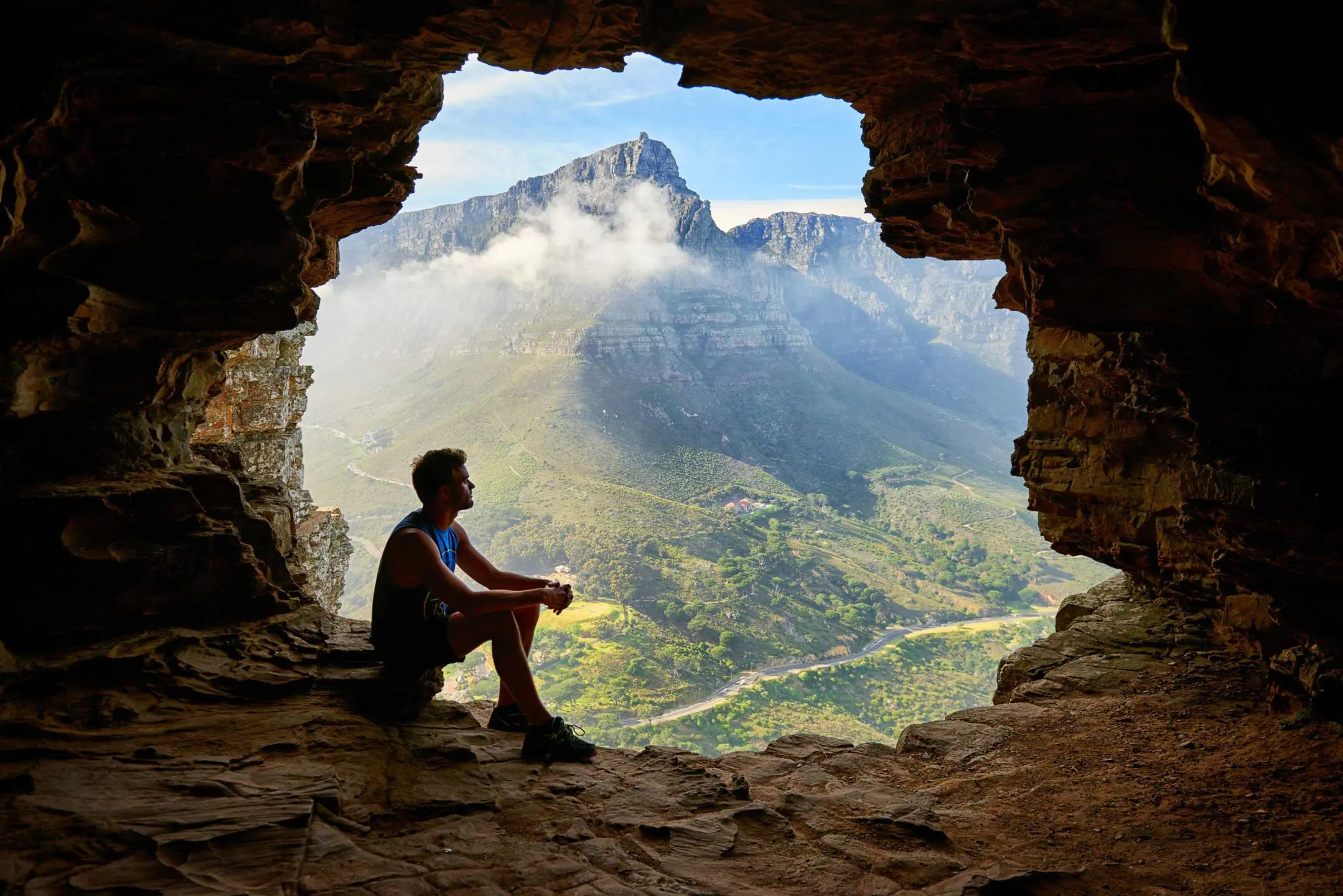 Man sitting in cave comtemplating mountain view